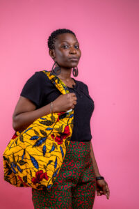 Femme portant un grand sac en tissu wax jaune à fleurs rouges et bleues sur l'épaule, création artisanale Nicole Wax.