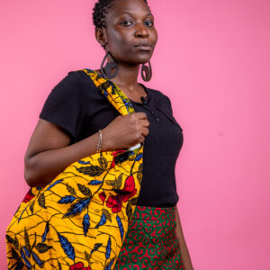 Femme portant un grand sac en tissu wax jaune à fleurs rouges et bleues sur l'épaule, création artisanale Nicole Wax.